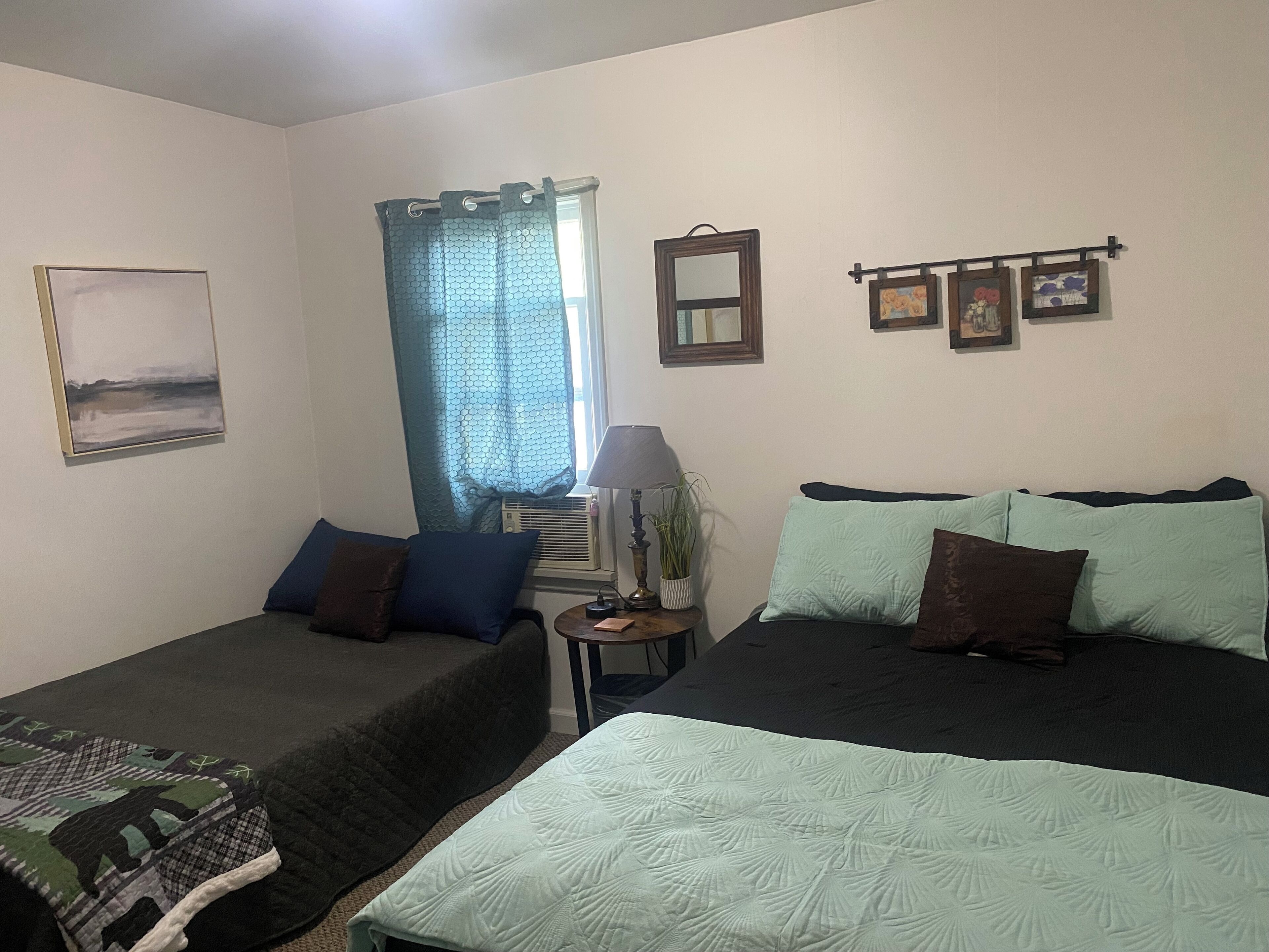 Quarto com duas camas, janela com cortinas, luminária, espelho e quadros nas paredes.