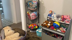 Un espace de jeux pour enfants avec un ours en peluche dans un panier, une étagère remplie de jouets en peluche et un mur décoré de tableaux.