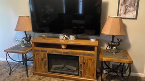Un salon avec un téléviseur à écran plat posé sur un meuble de télévision en bois, flanqué de deux tables d’appoint sur lesquelles se trouvent des lampes et des objets décoratifs.