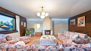 Una sala de estar acogedora con una chimenea de piedra, sofás con estampado floral, un televisor y obras de arte en las paredes.