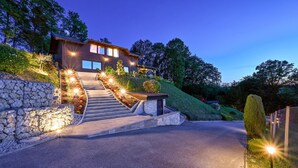 Una casa moderna con un muro de contención de piedra, una escalera de piedra e un camino de entrada bien iluminado.