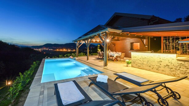 Zona junto a la piscina con sillones de descanso y un área de estar cubierta con vistas a un paisaje montañoso.