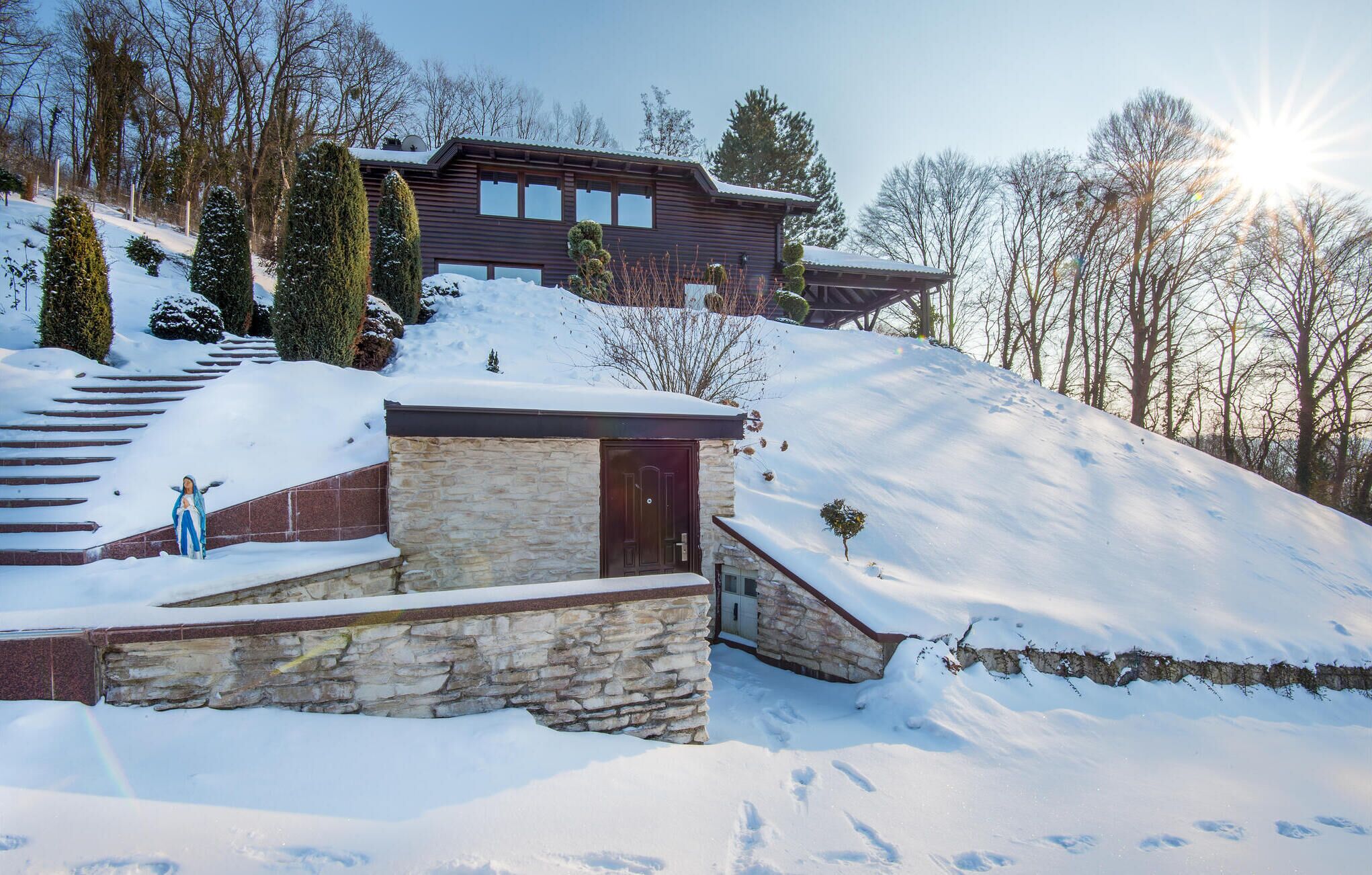 A modern house with a stone entrance, a wooden staircase, and a view of the surrounding snowy landscape.