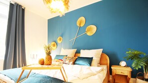 A well-lit bedroom with a bed, a bedside table with a clock, a small table with a pineapple and glasses, and a large potted plant. - ARTstudio 2.0 Superior 2-bedroom apartment with terrace. Near IGA 27! (Duisburg)