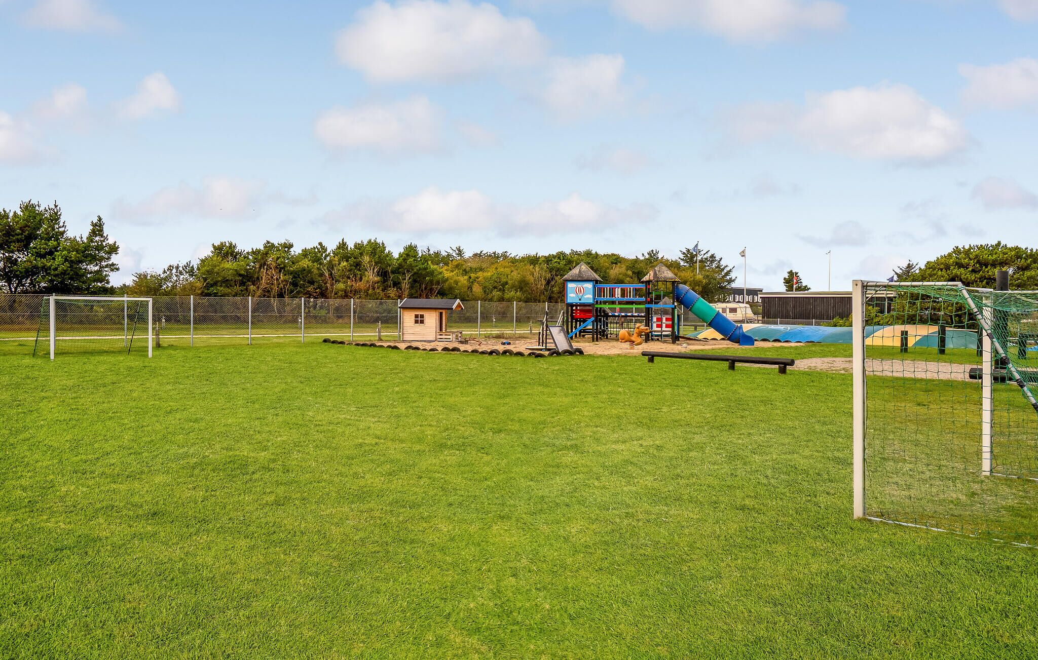 Ein eingezäunter Außenbereich mit einer kleinen Spielanlage, einer Rutsche und einem Fußballtor.
