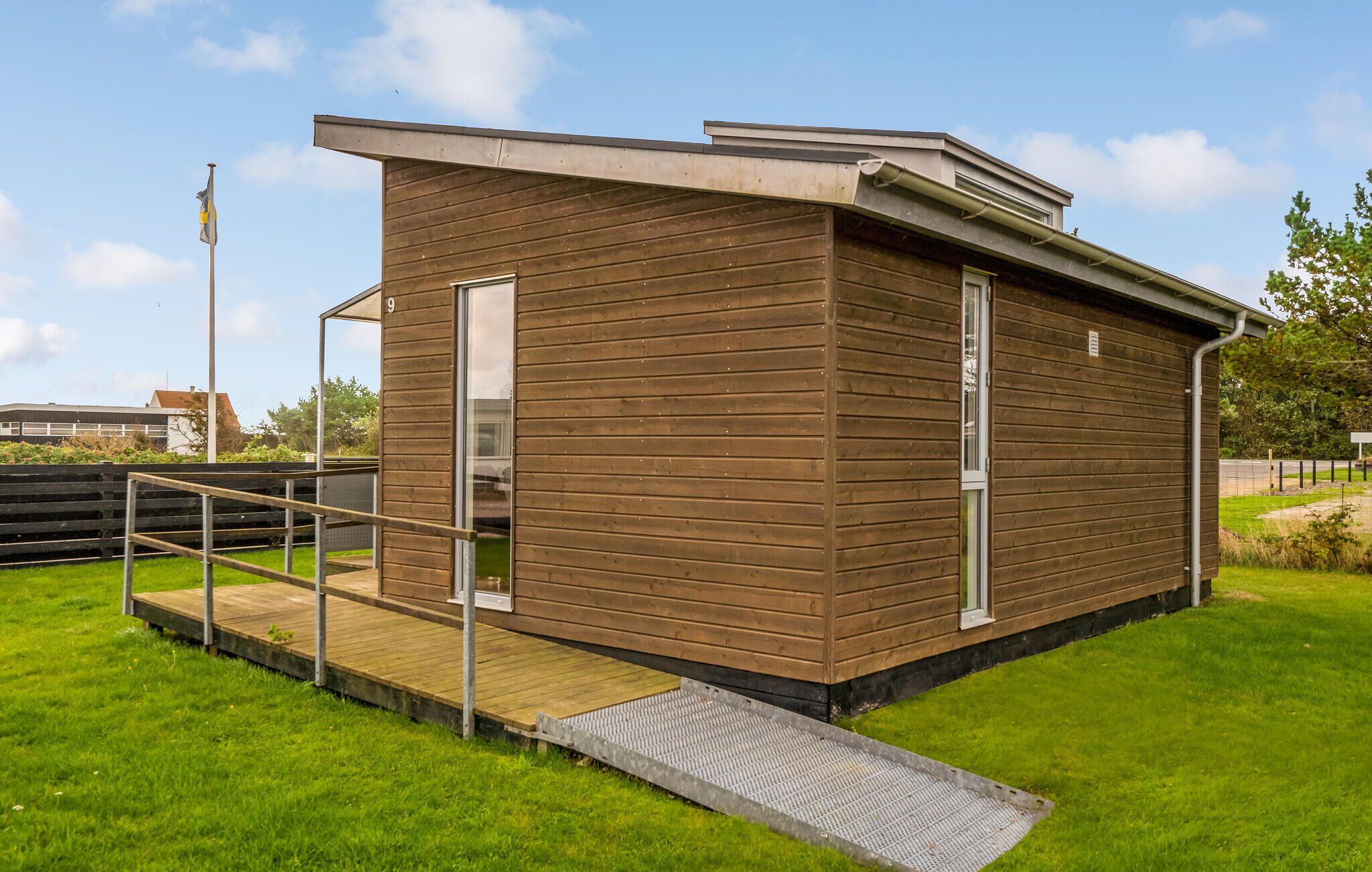 A small, single-story wooden building with a metal ramp and a door, number 9, in a grassy area with a clear sky.
