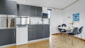 Una cocina moderna con armarios grises, horno integrado y comedor con mesa blanca y sillas negras.