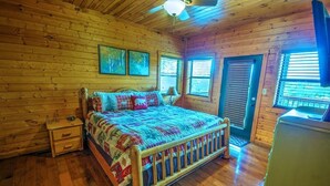 Ein Schlafzimmer einer Holzhütte mit einem Bett, Nachttischen, einem Deckenventilator und einer Tür.