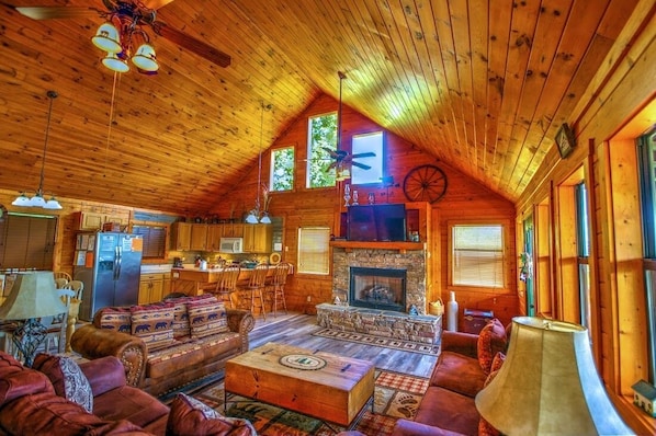 A cozy log cabin interior with a fireplace, wooden furniture, and a kitchen area. - Don't be shy...Visit the mountains! Amazing Views, King Bedrooms, Secluded. (Sevierville)
