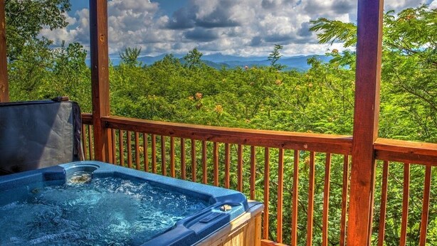 Ein Whirlpool auf einer Holzterrasse mit Blick auf eine üppige grüne Landschaft und Berge in der Ferne.