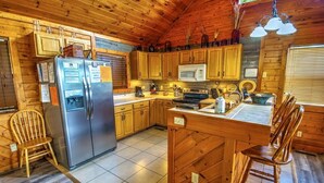Eine gemütliche Kücheneinrichtung im Chalet-Stil mit Holdekor, einem Edelstahl-Kühlschrank, einer Mikrowelle und einer zentralen Kochinsel mit Hockern.