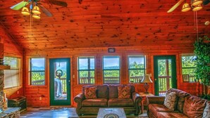 Ein Blockhaus-Interieur mit Holzbalkendecke, einer Couch, einem Couchtisch und Blick ins Freie durch große Fenster.