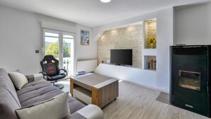 A modern living room with a sofa, a gaming chair, a coffee table, a TV mounted on a stone wall, and a black refrigerator.