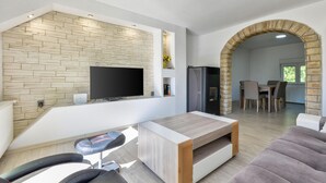 A modern living room with a stone wall, a flat-screen TV, a fireplace, and a dining area with natural light.