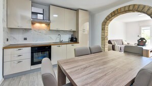 A modern kitchen with marble countertops, integrated appliances, and a dining area with a wooden table and chairs.
