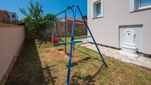 Ein Schaukelstuhl in einem Garten mit einer Steinmauer, einem kleinen Baum und einem weißen Gebäude mit einem Fenster.