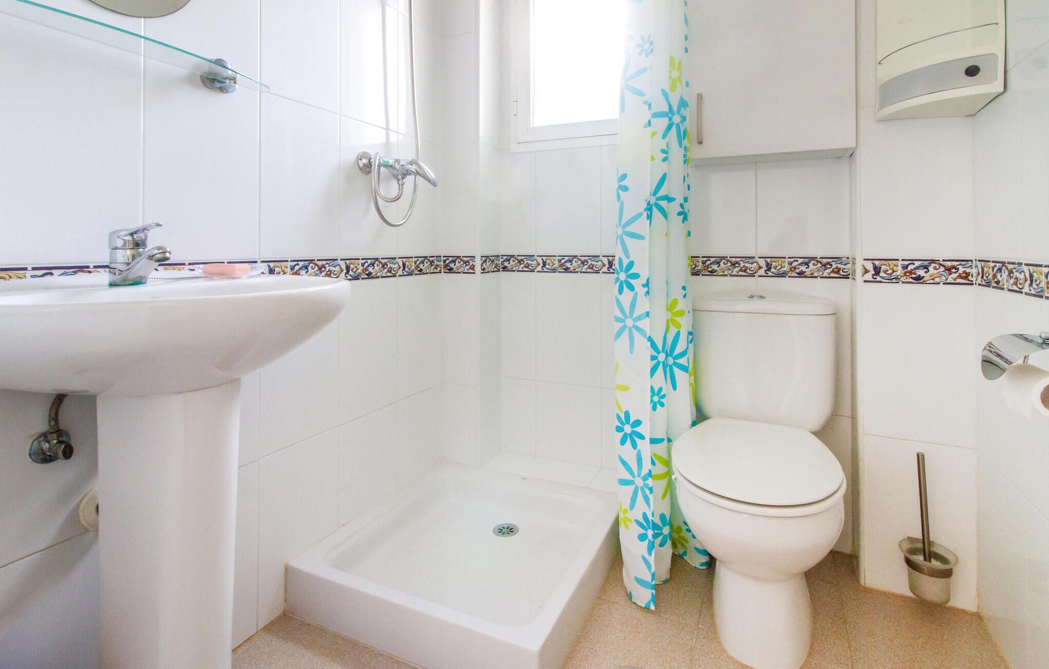 A bathroom with a sink, toilet, shower, and a window.