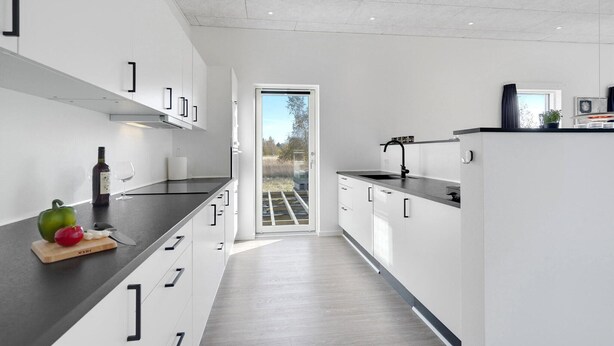 Eine moderne Küche mit weißen Schränken, einer dunklen Arbeitsplatte und Blick ins Freie durch eine offene Tür.