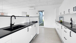 Eine moderne Küche mit weißen Schränken, schwarzen Arbeitsplatten und einem schwarzen Wasserhahn. Ein Fenster bietet Blick ins Freie.