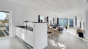 Eine moderne Küche mit einer Kochinsel, ein Essbereich mit Tisch und Stühlen sowie ein Wohnbereich mit Sofa und Fernseher.