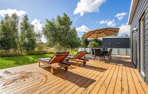 A wooden deck with two lounge chairs and a table, a barbecue grill, and a covered area with an umbrella. - 3 bedroom amazing home in Rødby (Rødby)