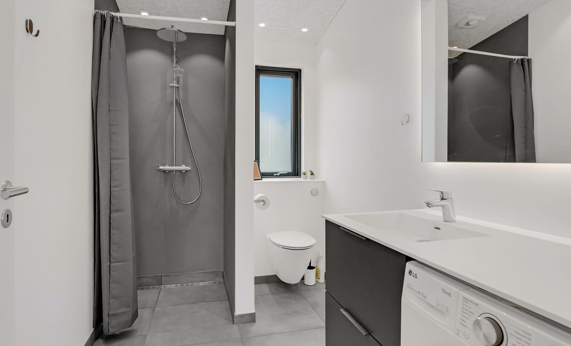 Ein modernes Badezimmer mit Dusche, Toilette und integriertem Waschmaschinenanschluss.