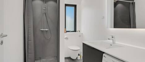Ein modernes Badezimmer mit Dusche, Toilette und integriertem Waschmaschinenanschluss.