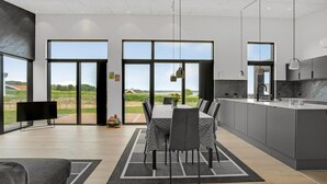 A modern kitchen with large windows, a dining area with a view, and a flat-screen TV. - Gorgeous home in Sjølund with kitchen (Sjølund)