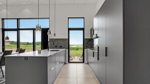 A modern kitchen with a large island, two pendant lights, and a view of a green landscape through a large window. - Gorgeous home in Sjølund with kitchen (Sjølund)