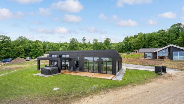 A modern two-story house with large glass windows, a patio with outdoor furniture, and a surrounding grassy area. - Gorgeous home in Sjølund with kitchen (Sjølund)