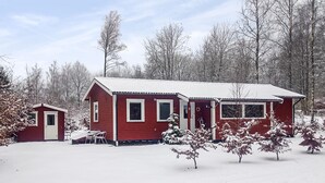 A red cabin with a small attached shed, surrounded by snow-covered trees. - Cozy home in Perstorp with WiFi (Perstorp)