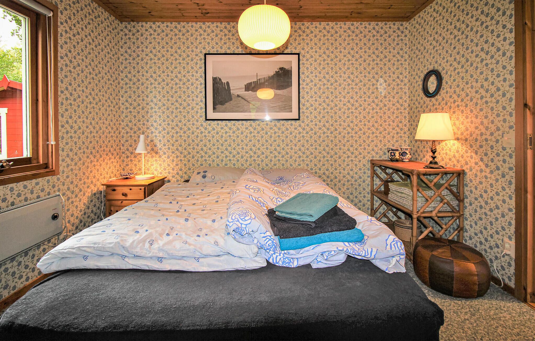 A bedroom with a bed, a nightstand, a lamp, a wall clock, and a framed picture.