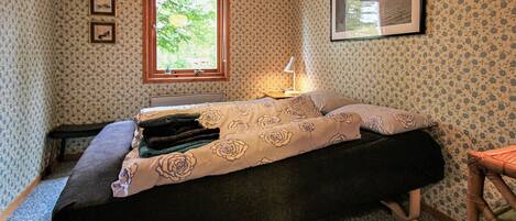 A bedroom with a bed, a window, a lamp, and a picture on the wall.