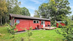 A red cabin with a deck, surrounded by trees and a grassy yard. - Cozy home in Perstorp with WiFi (Perstorp)