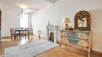 Une pièce comprenant une table à manger et des chaises, une cheminée agrémentée d’objets décoratifs, une commode avec un miroir et un lustre.