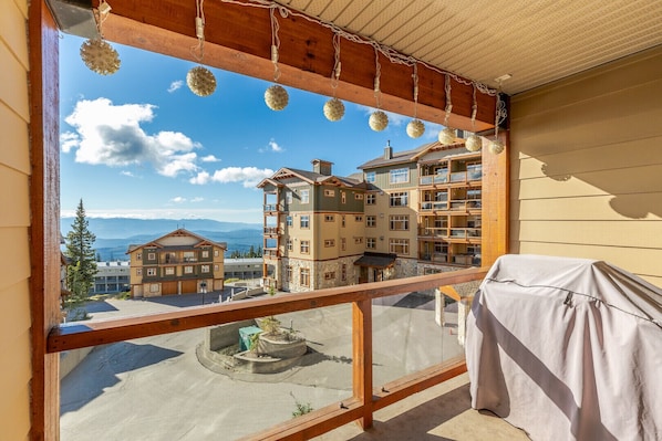 Un balcón con vistas a una zona montañosa, un área de estar al aire libre techada y un edificio con múltiples balcones y ventanas.