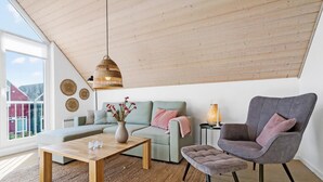 Uma sala de estar moderna com teto de madeira, um sofá, uma poltrona, uma mesa de centro e um lustre.