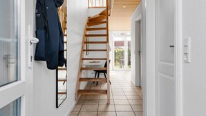 Um interior moderno com escada de madeira, porta branca e chão ladrilhado.
