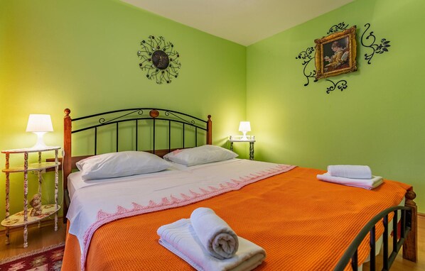 Un lit bien fait, avec une couvre-lit orange et des oreillers blancs, deux lampes de chevet, un élément décoratif mural et un tableau encadré.