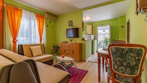 A living room with a sofa, a dining table with chairs, a TV, and a kitchen area with a refrigerator. - 1 bedroom beach front apartment in Premantura (Premantura)