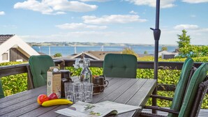 A wooden table with a view of the sea, green chairs, a bottle, glasses, and a menu. - 4 bedroom cozy home in Rønde (Rønde)