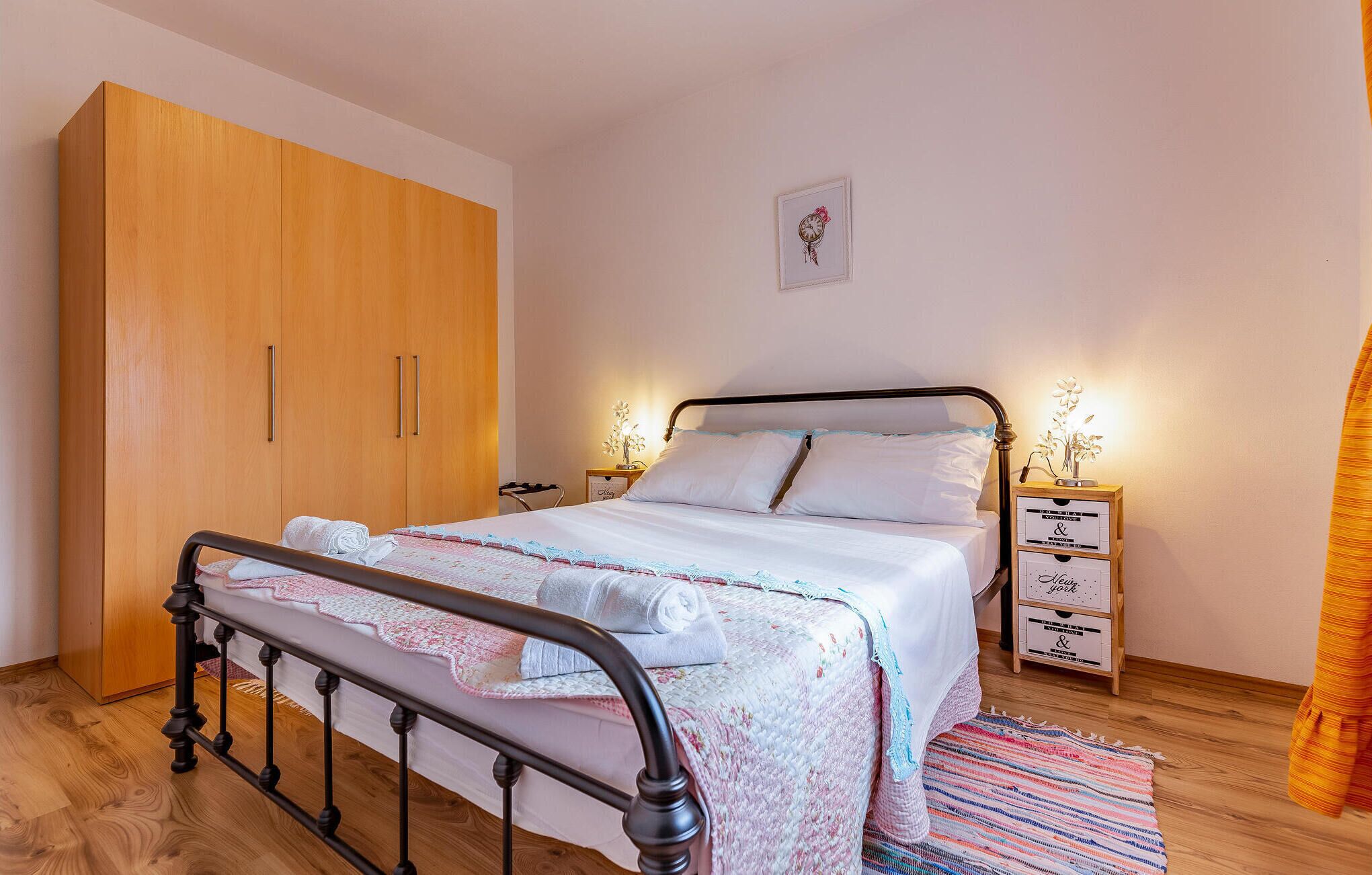 A bedroom with a bed, wooden wardrobe, bedside tables, and a wall clock.