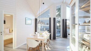 A modern, open-plan living space with a wooden interior, a dining area with white chairs, and large windows offering views of the outdoors. - Amazing home in Krems II/Warderbrück with sauna (Krems II/Warderbrück)