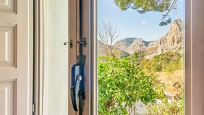 A door with a view of a mountainous landscape and a tree in the foreground.