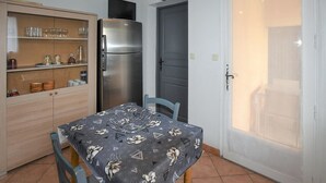 A compact kitchen with a refrigerator, a dining table with chairs, and a door with a clock. - Amazing home in Avignon (Avignon)