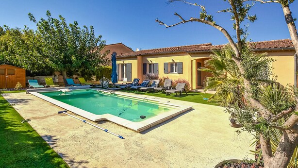 A rectangular swimming pool with a surrounding deck, a lawn, and a building with a tiled roof in the background. - Amazing home in Avignon (Avignon)