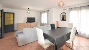 A modern living room with a sofa, a dining table with chairs, a TV on a wooden cabinet, and a large window with curtains. - Amazing home in Avignon (Avignon)