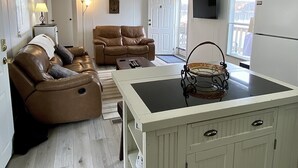A cozy living room with a brown leather sofa, a white coffee table, and a kitchen area with a white island and cabinets. - Waterfront River Home (Harpers Ferry)
