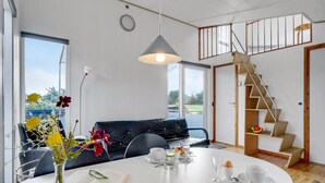Ein modernes Wohnzimmer mit einem schwarzen Ledersofa, einem Esstisch mit Frühstücksutensilien und einer Treppe mit Holzbalken.