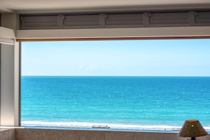 A view of the ocean through a large window, with a lamp on the windowsill.